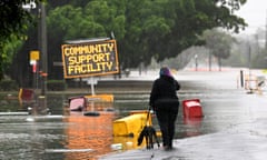 Woman walking near a flooded road and a portable sign that reads 'community support facility'