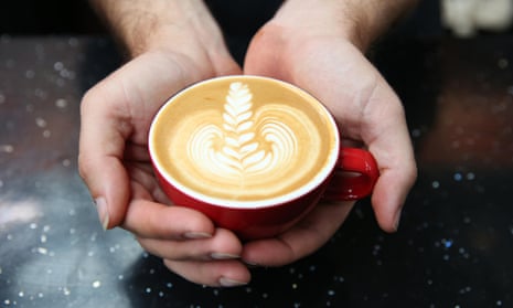 Cupped hands holding a coffee cup with latte art on the surface