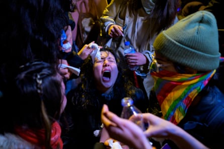 A woman screams with pain as other women try to help wash the chemical out of her eyes