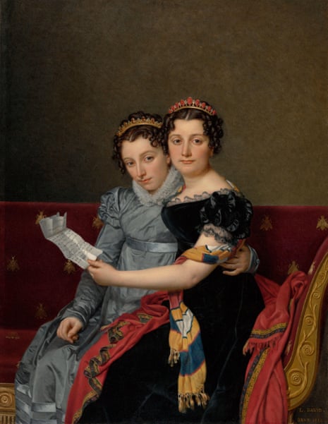 Two tiara-wearing women embrace as they read a letter