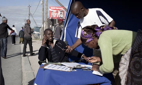 An employee of a bank checks an identity document via mobile phone as he sells accounts on the street in Khayelitsha, a township outside Cape Town, South Africa