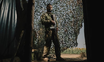 Vladyslav Vasyliev stands in the shade of a makeshift camp, holding a weapon