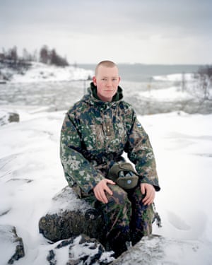 a man in camouflage gear sits on a stone in a snowy landscape