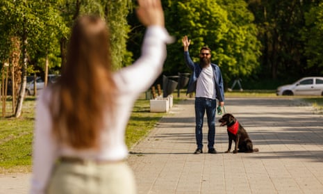 Couple meeting at the park to walk the dog, standing apart and waving at each other.