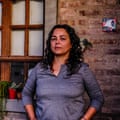 A woman wearing a grey shirt standss on front of a house.