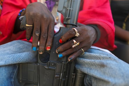 A closeup of a pair of hands, wearing jewellery, whole holding a rifle