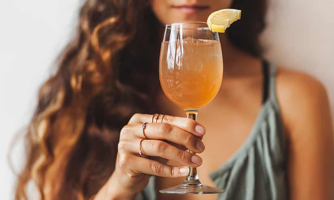 Partial view of woman holding wine glass of something light orange with lemon on the side