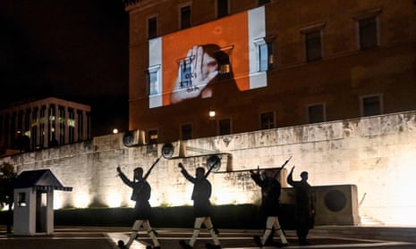 Presidential guards walk past a projection on the Greek parliament building in Athens reading “No to violence” for the International Day for the Elimination of Violence Against Women