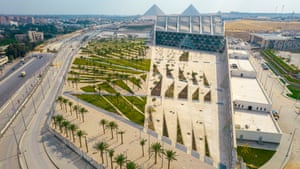 an aerial view of the Grand Egyptian Museum complex with two towering pyramids in the distance