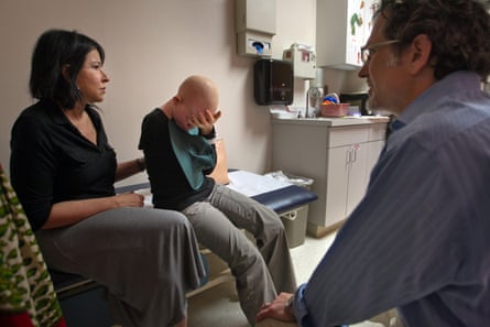 A white woman sits comforting a one-armed young African woman with albinism, who has her face in her hands, while a white man talks to them