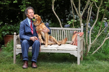 Monty Don in a suit sitting on a bench with a golden retriever