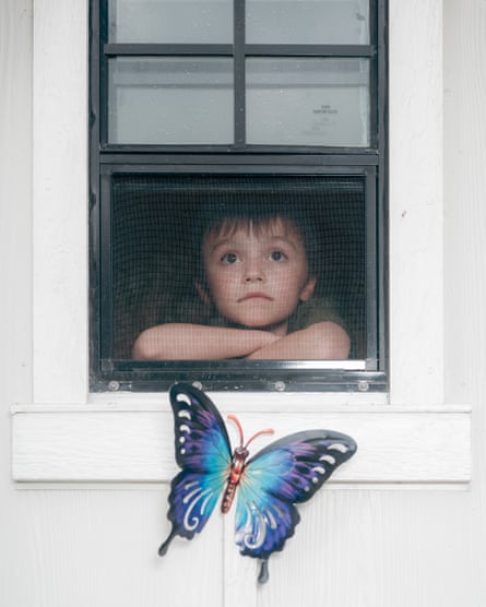 A child looks out out of a screened window with a butterfly decoration under it