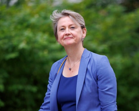 Yvette Cooper smiles in a blue blazer, standing outdoors in front of greenery