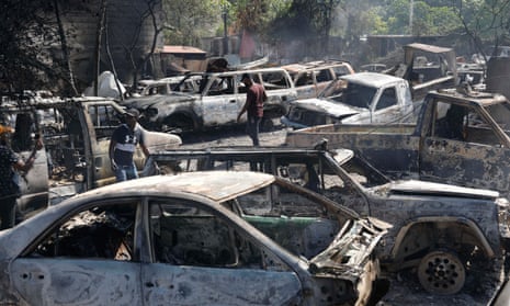 People look for salvageable pieces from burned cars at a shop that was set on fire by armed gangs in Port-au-Prince, on Monday, 25 March 2024.