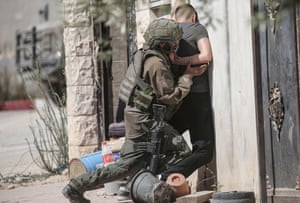 An Israeli soldier pushes a young Palestinian man up against a wall