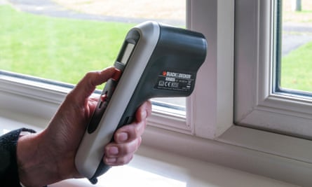 A person holding a thermal leak detector up to a window.