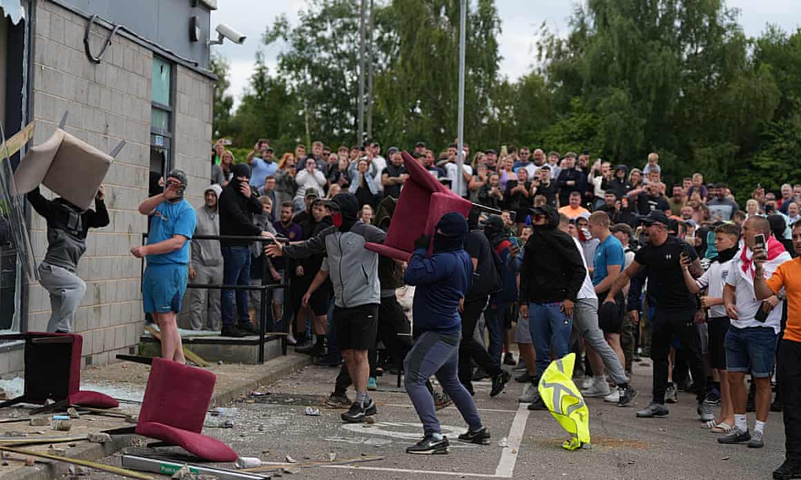 People throw chairs at a hotel building that has smashed windows, as a crowd behind look on