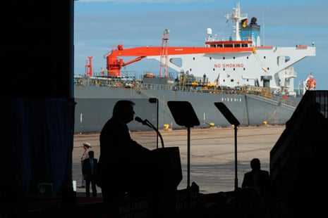 President Trump silhouetted speaking at a podium, with an oil tanker ship behind him