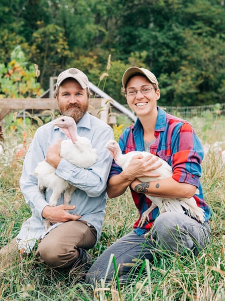 A man and a woman kneel in the grass holding turkeys in their arms.