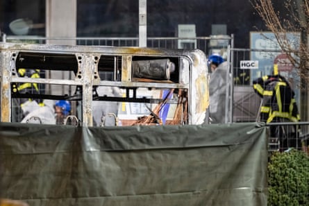 charred shell of a bus partially hidden by a plastic sheet
