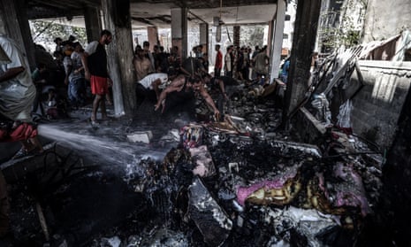 People stand among charred wreckage whilst a member of the civil defence team sprays water from a hose