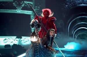 Lady Gaga performs sitting in a boat rowed by a figure in a fantastical red costume