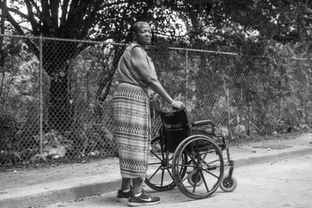a woman somberly pushes an empty wheelchair on the street