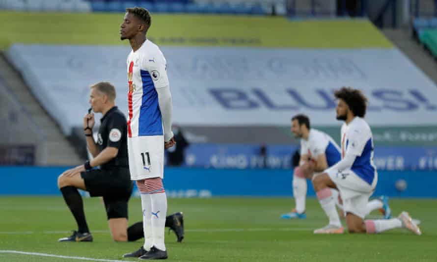 Crystal Palace's Wilfried Zaha stands up as others kneel in Leicester in April.  He feels that kneeling is not enough anti-racist action.