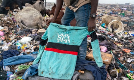 person sorts through discarded clothing in rubbish dump