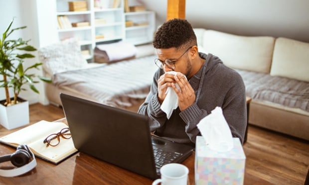 A man sitting at a table indoors blows his nose