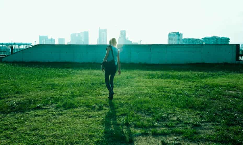 Teen girl walking across grass, urban skyline in background