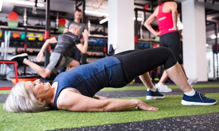 A silver-haired woman in the gym holding a simple bridge pose.
