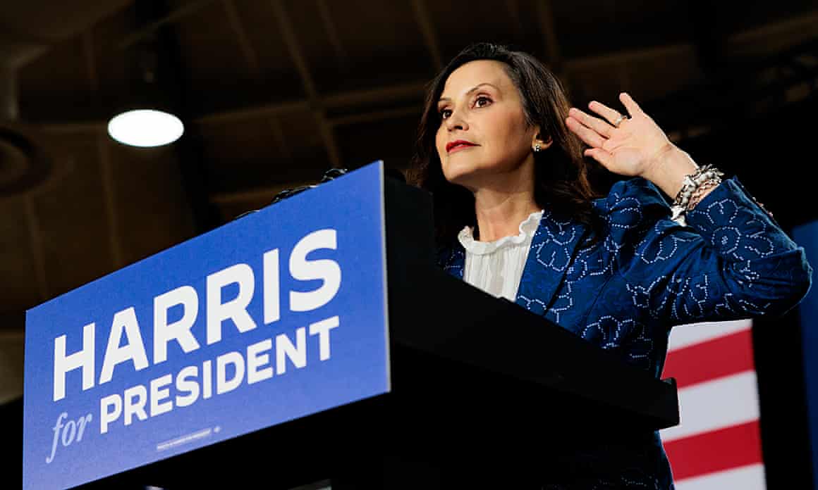 Whitmer gestures behind a lectern on which is written ‘Harris for president’