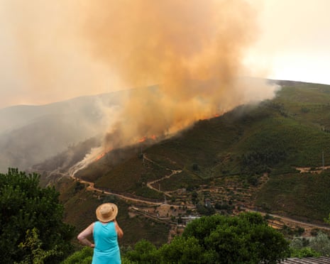 A woman watches as smoke billows from a forested area during a wildfire in the municipality of Arganil, central Portugal.