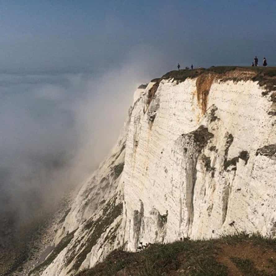 People stand on a cliff at Beachy Head amidst mist, near Eastbourne.