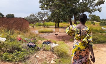 A woman stands facing some standing water, surrounded by washing spread out to dry.