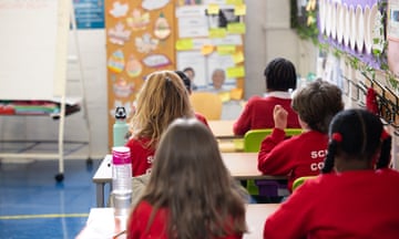 Four primary school children photographed from behind, sitting at desks in a classroom