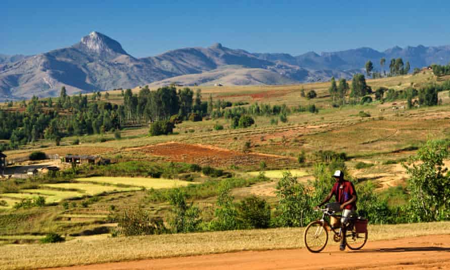 A beautiful valley landscape with mountains in the distance, and a man cycling along a dirt road in the foreground