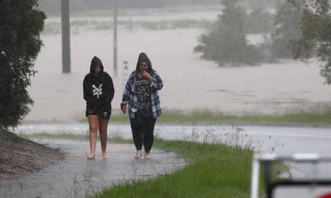 People in rain near a flooded road in Logan. South-east Queensland residents are facing more intense rain and life-threatening flash floods as one of the most severe weather systems in a decade pummels the region.