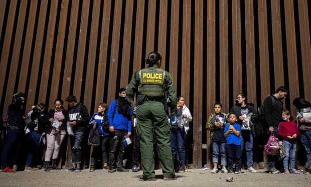 A US border patrol looks on at people wait to have their identities checked and taken to a processing center in Yuma, Arizona, in June.
