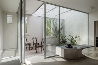 Glass sliding doors open onto a courtyard with white brick walls, plants and bentwood chairs
