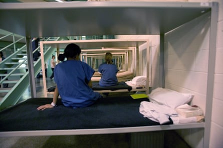 Seen from behind, women in blue shirts on a row of bottom bunks.