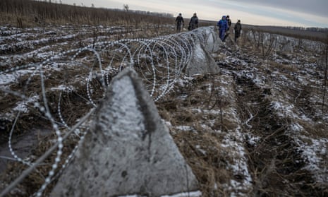 Workers walk along installed razor wire, a part of defence structures near a frontline in the Kharkiv region