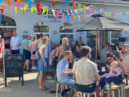People sit outside the bunting-clad distillery on wooden stools