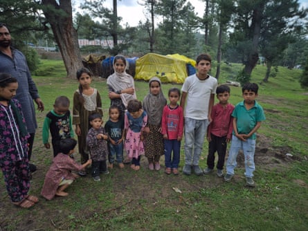 A southbound Asian man opinionated by 13 young children and toddlers amid immoderate conifer trees pinch a crude shelter successful nan background