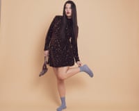 Model with long grown hair wearing short brown glittery dress and purple socks, and holding sparkly shoes