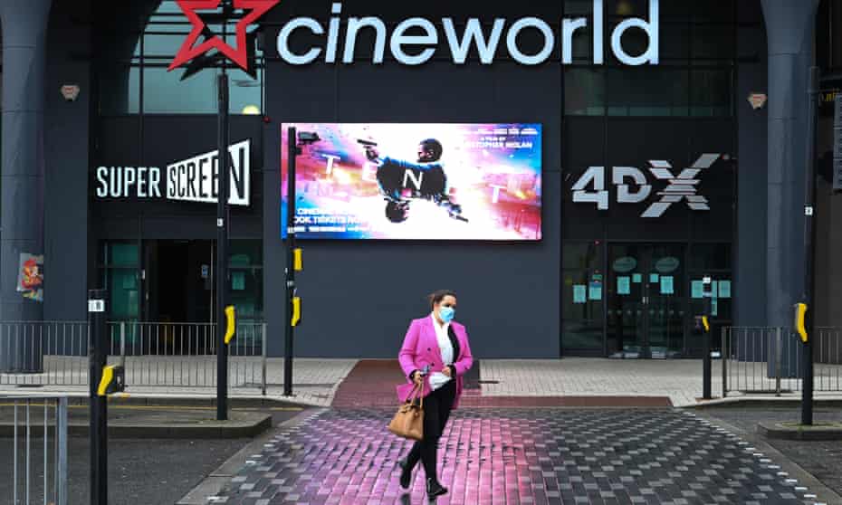 A woman wears a surgical face mask as she crosses the road in front of a Cineworld cinema in Cardiff