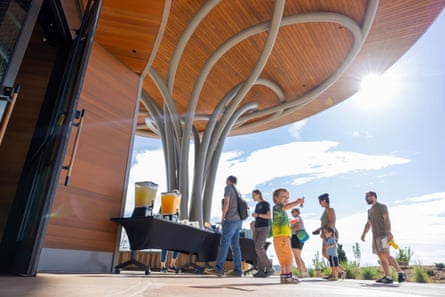 People queue at an outside drinks stall next to a modern public building.
