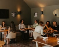 Diners chat around wooden tables in a low-lit room at Kintsu restaurant