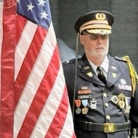 a man in a military uniform stands next to a US flag
